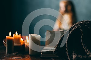 On the old vintage wooden table is a candlestick with candles. A red-haired girl in vintage clothes is sitting at the table, readi