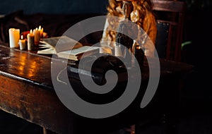 On the old vintage wooden table is a candlestick with candles. A red-haired girl in vintage clothes is sitting at the table, readi