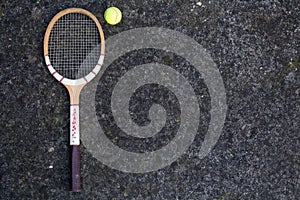 Old vintage wooden tennis racket on isolated stone background with green ball.