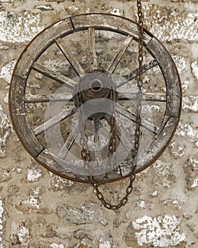 Old vintage wooden wheel with rusty metal chain hanging on a stone house wall