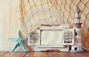 Old vintage wooden white frame and lighthouse on wooden table. vintage filtered image. nautical lifestyle concept
