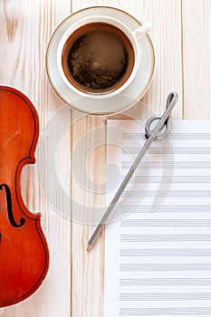 Old violin, pencil treble clef shape, musik note paper and cup of coffee.. Top view, close up, flat lay on white wooden background