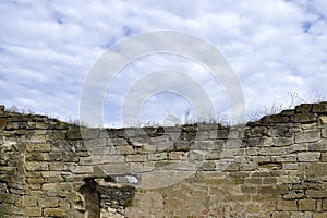 An old wall of an ancient stone building destroyed by time with dry grass on the background of a cloudy sky. Copy space.