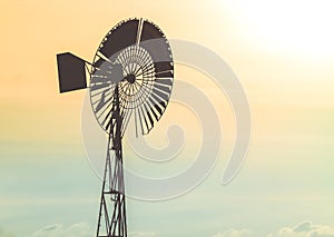 Old water pumping windmill in the sky at sunset