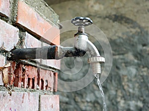 Old water tap with running water on bricked wall,  drinking water is flowing from the faucet, outdoor, close up