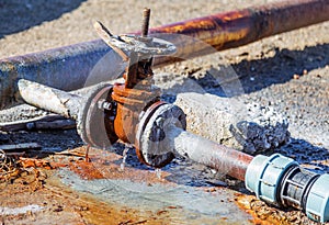 Old water valve. An rusty water valve in a puddle of flowing water. Large and rusty faulty leaking valve in close-up of an outdoor