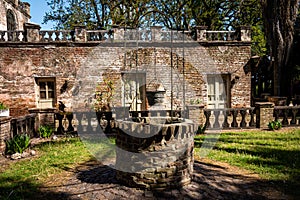 Old water well made of bricks and cobblestone surrounded by an abandoned house