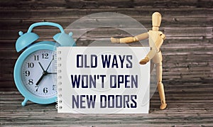 Old ways won`t open new doors. Motivational quote on a notepad, a clock and a wooden doll on a brown background. Inspirational