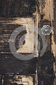 Old weathered antique beat-up wood panel door with chipped peeling paint and black porcelain doorknob and rusty plate