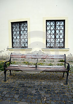 Old weathered bench with two windows behind on a street