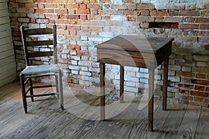 Old weathered brick interior wall of building with pieces missing, a weathered chair and table set on corner of wood floor