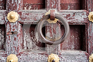 Old, weathered doorknocker ring handle on an ancient wooden door with peeling paint