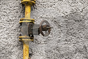 Old weathered gas crane and pipe on the background of a gray wall. Old gas gate of yellow colour is on a pipe and blocks