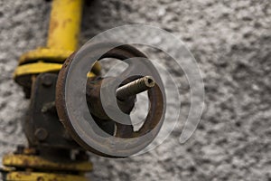 Old weathered gas crane and pipe on the background of a gray wall. Old gas gate of yellow colour is on a pipe and blocks