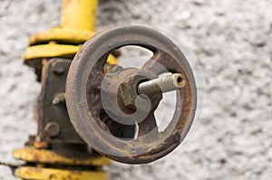 Old weathered gas crane and pipe on the background of a gray wall. Old gas gate of yellow colour is on a pipe and blocks