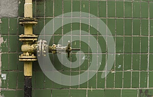 Old weathered gas crane and pipe on the background of a green wall. Old gas gate of yellow colour is on a pipe and