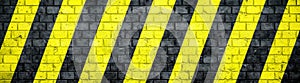 Old and weathered grungy brick wall with danger or attention black and yellow warning diagonal stripes texture background banner