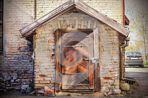 Old weathered locked vintage wooden door with padlock in small brick house entrance