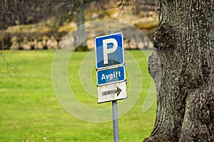 Old and weathered parking sign by a tree..