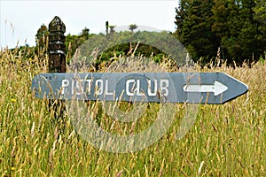 Old weathered Pistol club sign in a field of grass