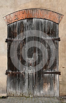 Old weathered rotten wooden dark door in a n old brick wall.