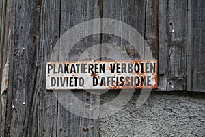 old weathered and rusted enamel sign in German and Italian against a wooden wall. Text reads \