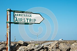 Old weathered sign airstrip in English and Irish language by a stone fence. Travel and tourism concept. Blue sky in the background