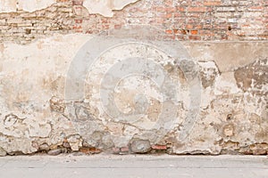 Old weathered vintage brick wall with broken plaster and pavement on the ground. Grungy urban background. photo