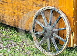 Old weathered wagon wheel with wooden spokes leaning against a yellow wooden box