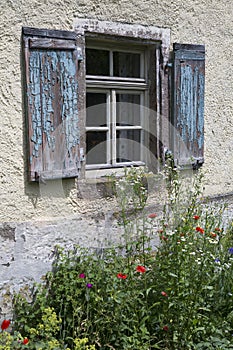 Old weathered window with wooden shutters with a flower garden