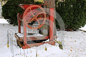 Old weathered wine press set next to tall tree under fresh snow