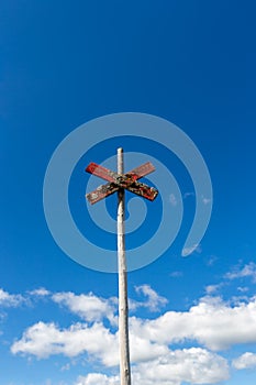 Old weathered wooden trail sign post with red cross against blue sky with clouds.