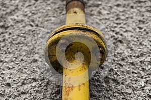 Old weathered yellow gas pipe on the background of a gray wall.