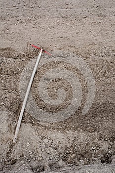 Old weeding tool or rake abandoned lying in garden on soil. Vert