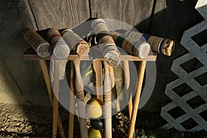 Old well-used Croquet mallets in a rack leaning against a wooden wall, at a downward angle