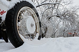 Old wheel with spokes in the snow. Close up vintage white car wheel over snow cover in winter time