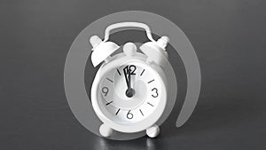 Old white alarm clock with black numbers and arrows on a black background. Timelapse close-up white clock start time 11.55 hours 5