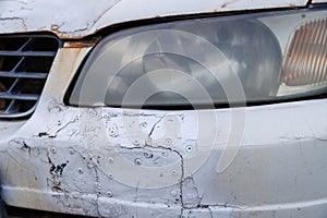 old white car bumper neglectly fixed with patches and rivetts and painted over with can of spraypaint, closeup view photo