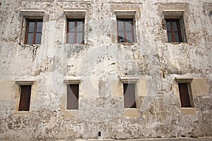 Old white cement wall with closed wooden windows.