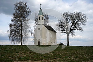 Old white chapel surrounded by trees under the cloudy sky