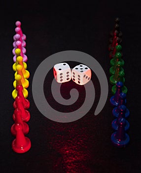 Old white dices in middle of color pawns in vertical align iluminated with red and white lights photo
