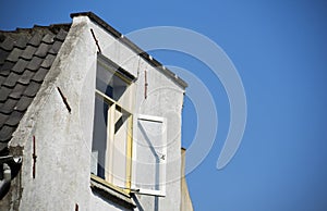 A old white dutch building roof with open shutters and a white framed glass window with a clear blue sky background