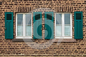 Old white framed windows on mediterranean house out of brick walls with green shutters