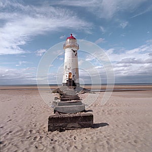 An old white lighthouse with a red roof on a sandy beach with the sea and sky in the background