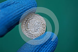 Old white medieval silver coin in fingers in blue gloves