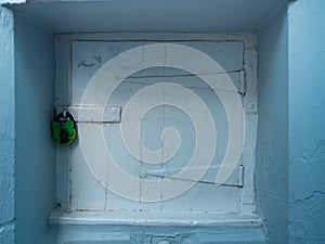 Old white painted hatch recessed into a blue wall.  Secured with a painted green padlock
