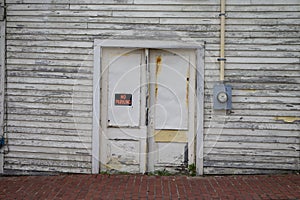Old white painted wood building and doors with sign with no parking text on it and brick walkway