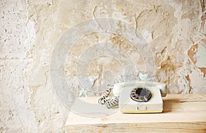 Old white retro telephone with dial black color plate on raw wooden board