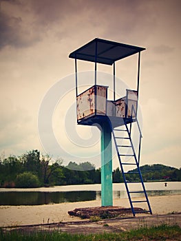 An old white and rusty metal lifeguard tower with chair on a lake beach.