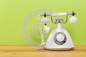 Old white telephone on wooden table with color wall background